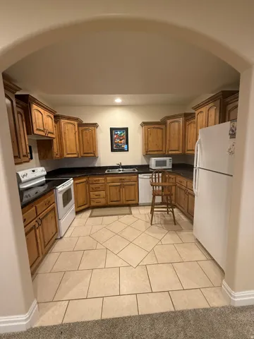 Basement Kitchen with wood finish cabinetry, white appliances, light tile patterned floors, and recessed lighting