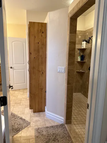 Bathroom with a tile shower, a textured wall, light tile patterned flooring, and a textured ceiling