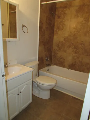 Bathroom featuring vanity, shower / tub combination, and dark tile patterned flooring