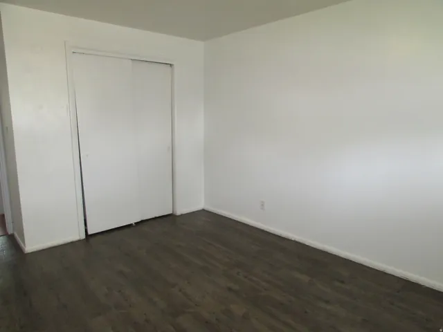 Unfurnished bedroom featuring dark wood-style flooring and a closet