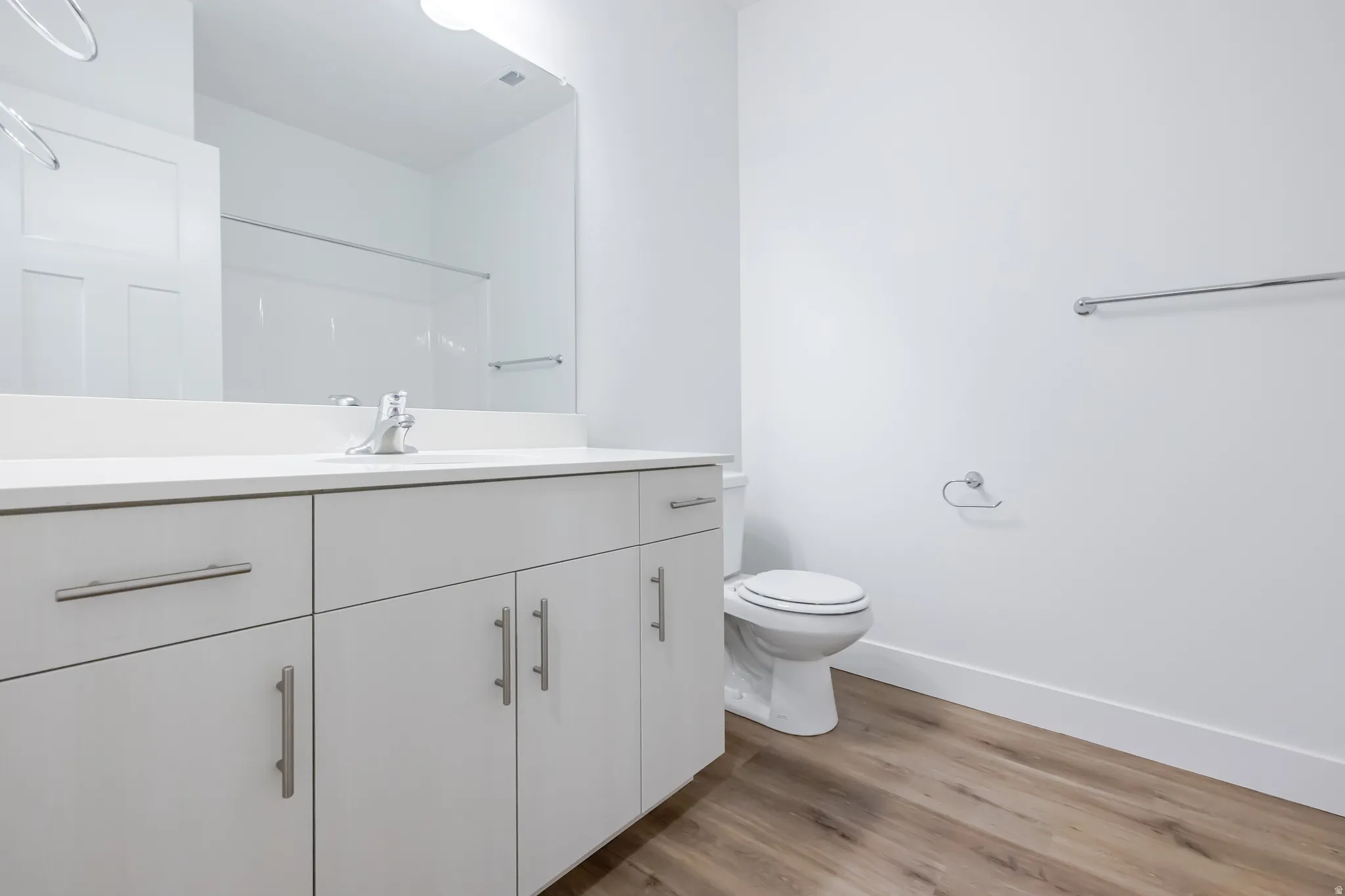 White vanity with brushed nickel hardware, integrated sink, wood-finish flooring, and a white toilet