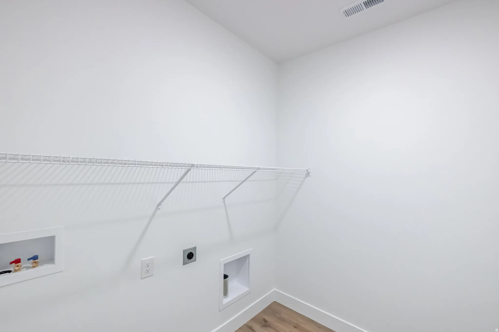 Laundry area with a wire shelf, wall-mounted electrical outlet, and wood-finish flooring