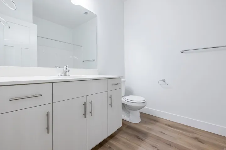 White vanity with brushed nickel hardware, integrated sink, wood-finish flooring, and a white toilet
