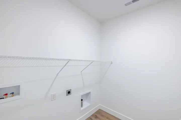 Laundry area with a wire shelf, wall-mounted electrical outlet, and wood-finish flooring