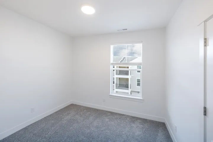 Recessed ceiling light fixture, white walls, gray carpet, window with blinds, white trim