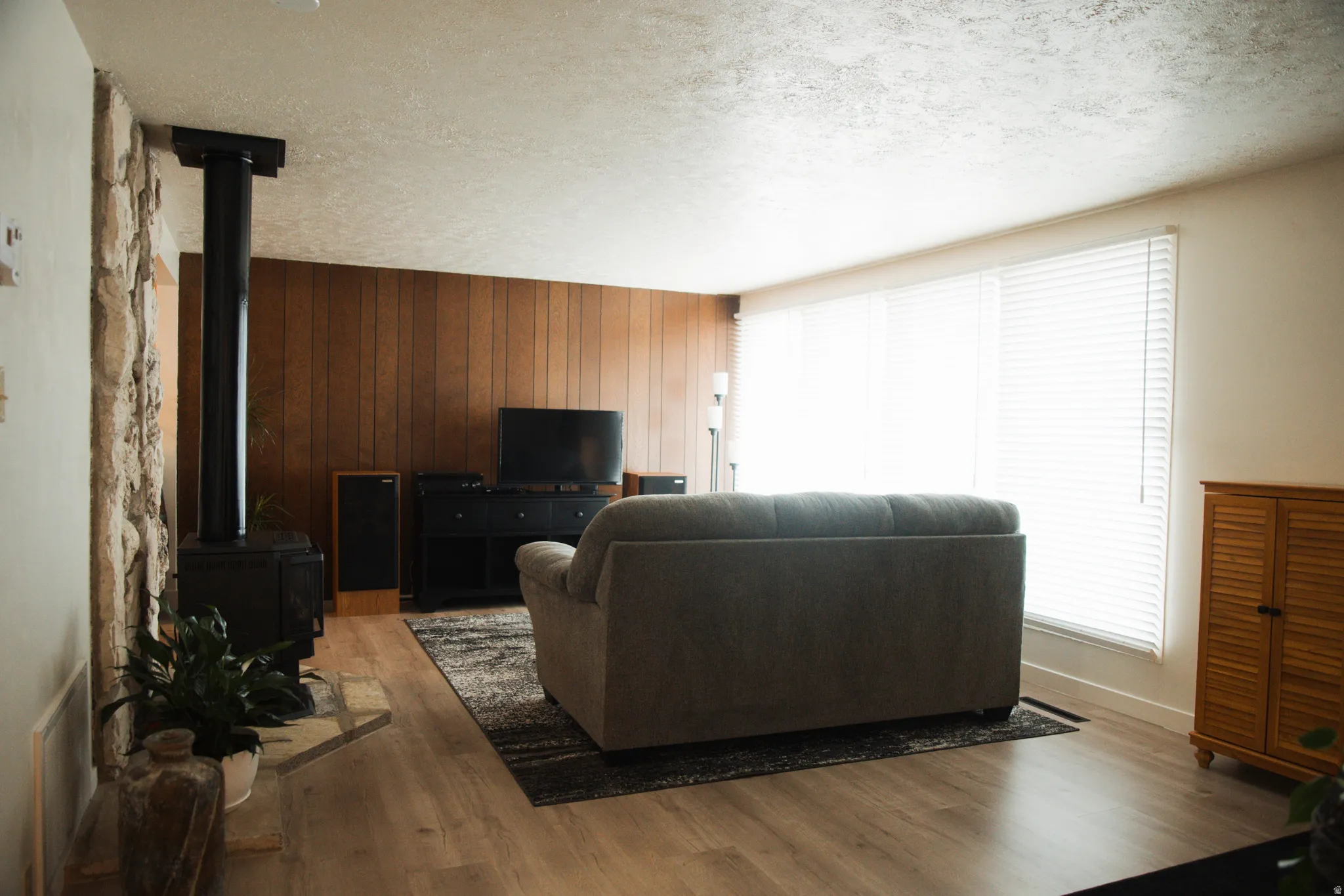 Living area with wooden walls, wood finished floors, a textured ceiling, and a wood stove