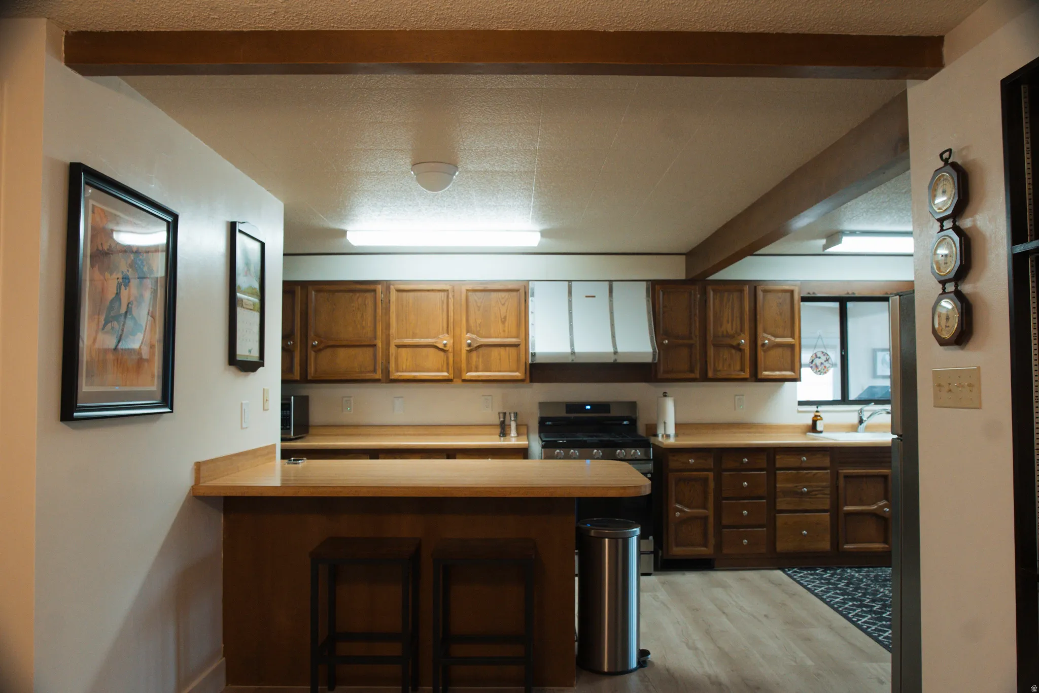 Kitchen with a breakfast bar area, wood finish cabinets, light countertops, a peninsula, and stainless steel appliances