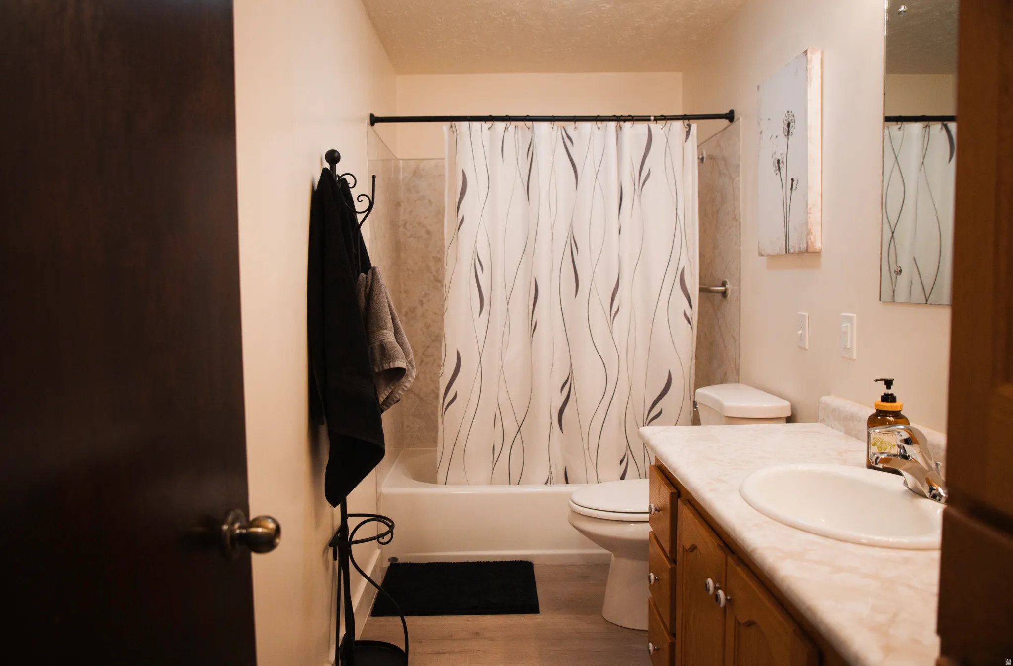 Full bath featuring a textured ceiling, vanity, shower / bath combination with curtain, and LVP flooring