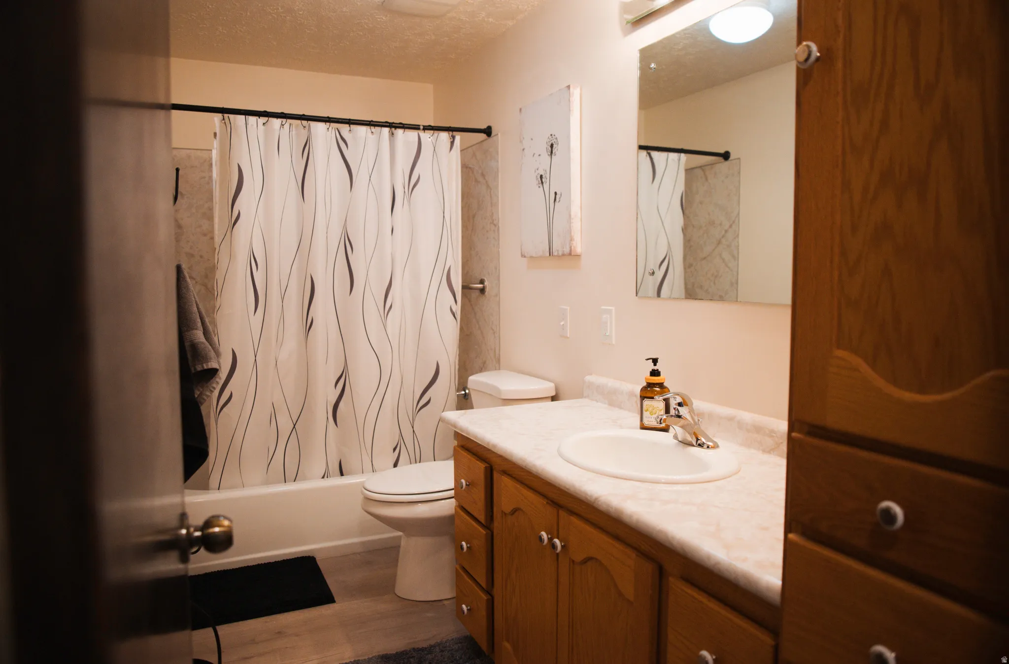 Bathroom with vanity, a textured ceiling, shower / bath combination with curtain, and LVP flooring.