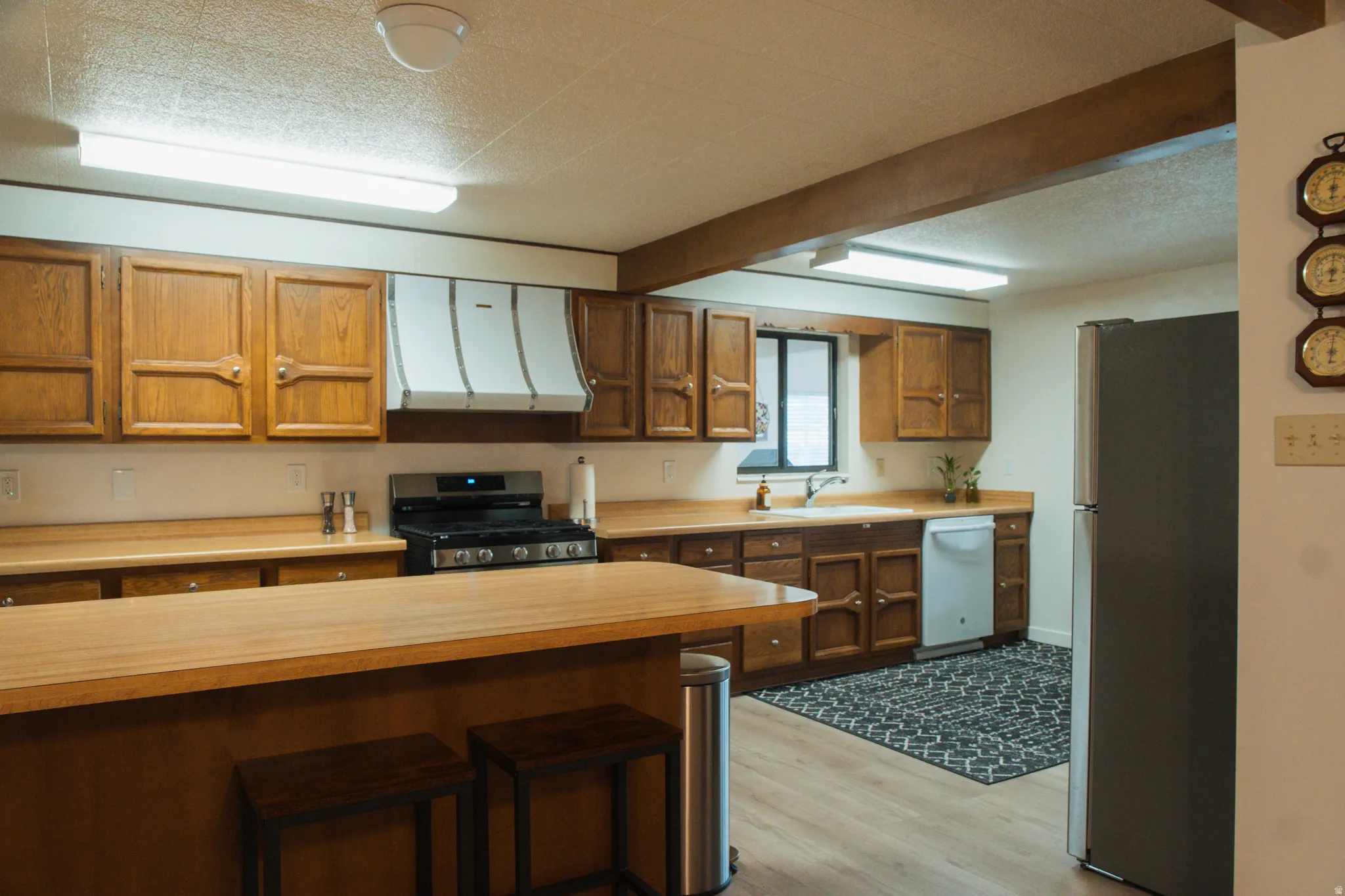 Kitchen with light countertops, stainless steel appliances, wood finish cabinetry, a textured ceiling, and light wood-style flooring