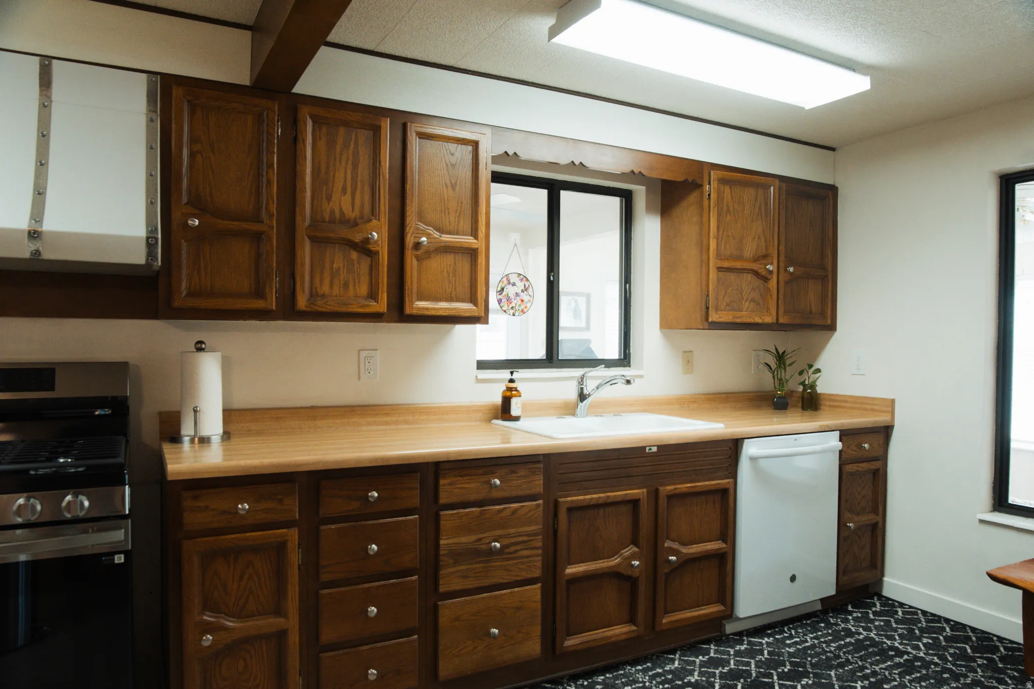 Kitchen with stainless steel gas range oven, light countertops, white dishwasher, and exhaust hood