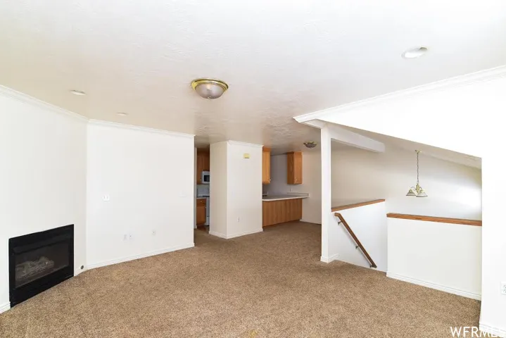 Unfurnished living room featuring crown molding, a glass covered fireplace, and light carpet