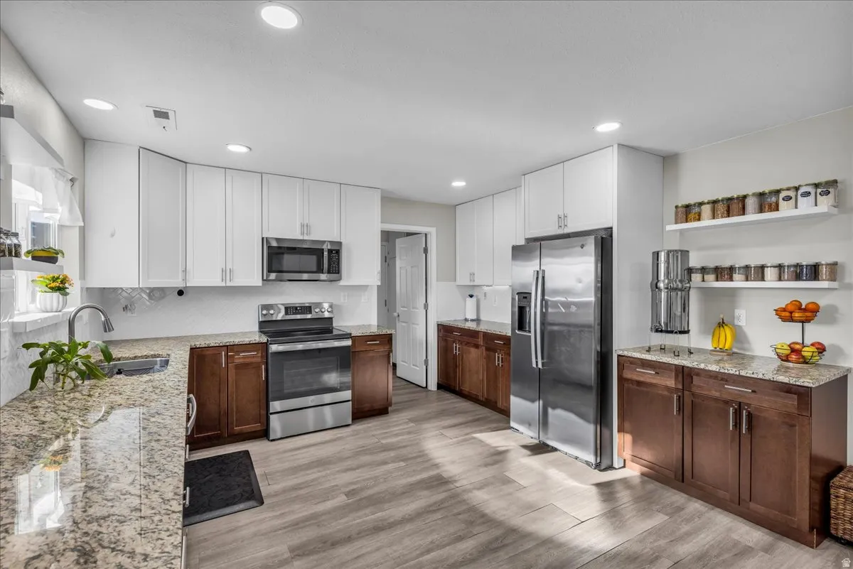 Two tone kitchen featuring two tone cabinets, open shelves, light stone counters, stainless steel appliances, and light wood-type flooring