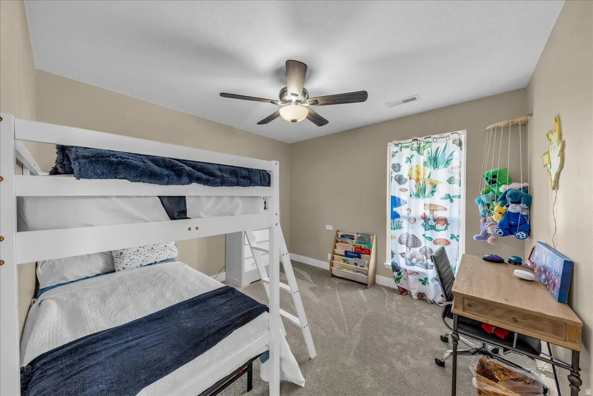 Bedroom with ceiling fan, light colored carpet, and a desk