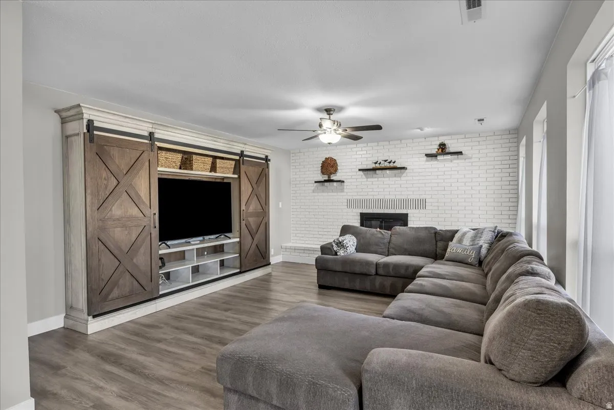 Living room with a barn door, brick wall, wood finished floors, a ceiling fan, and a fireplace