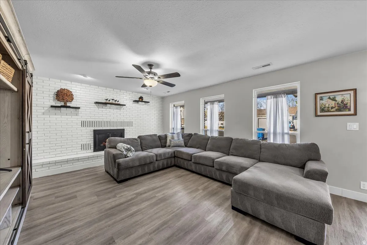 Living area featuring brick wall, wood finished floors, a textured ceiling, a fireplace, and ceiling fan