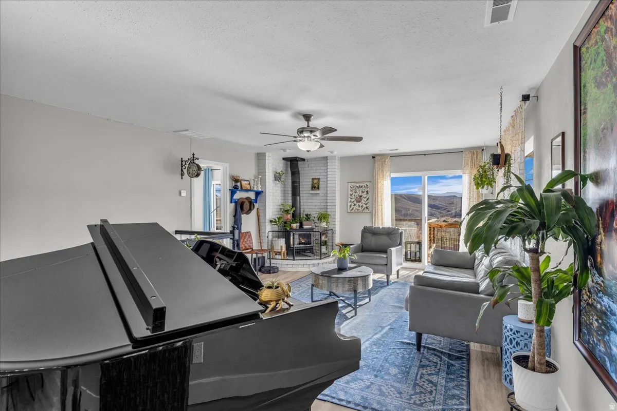 Living area with a wood stove, ceiling fan, wood finished floors, a mountain view, and a textured ceiling