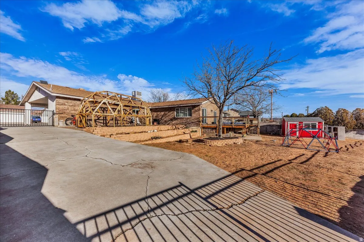 View of front of property with a shed, a gate, a patio, and concrete driveway