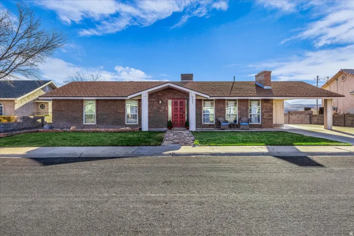 Ranch-style house featuring a chimney, a carport, brick siding, and driveway