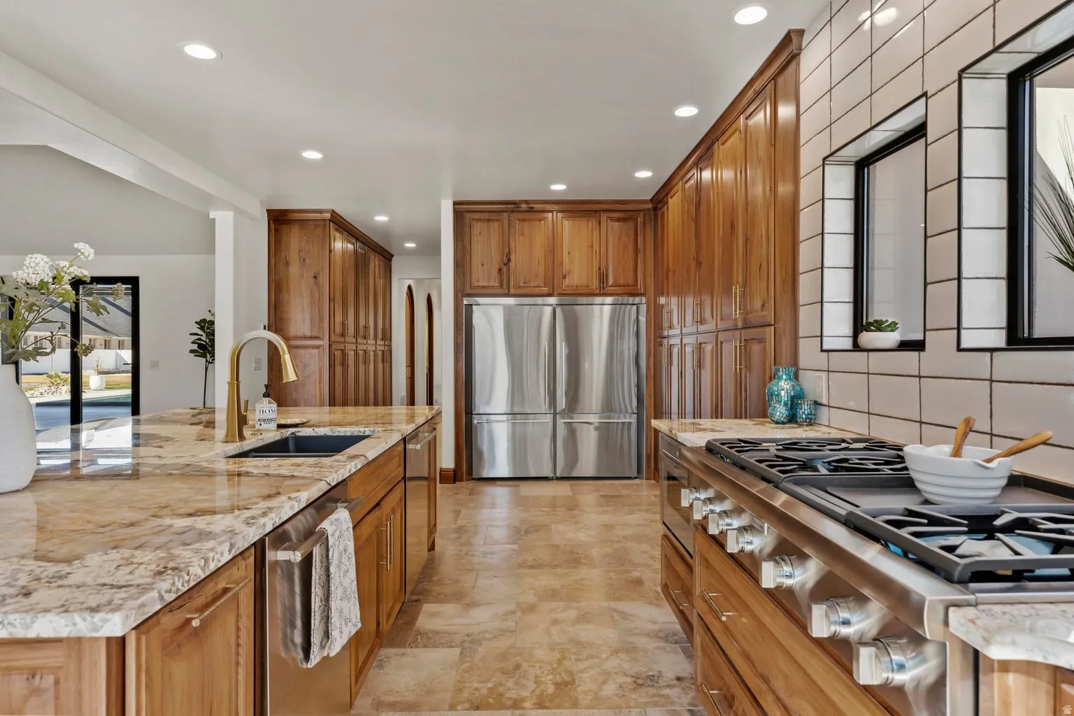 Kitchen featuring wood finish cabinets, stainless steel appliances, recessed lighting, light stone counters, and a center island with sink