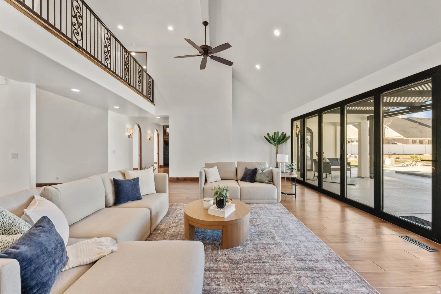 Living room with wood finished floors, recessed lighting, ceiling fan, sliding panel doors and vaulted ceiling