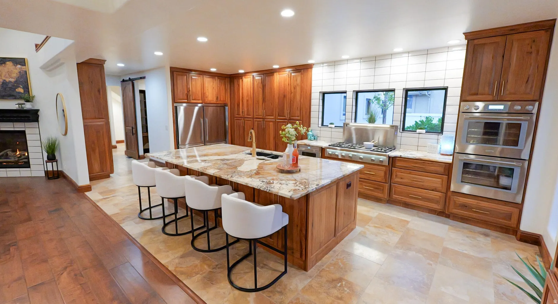 Kitchen featuring wood finish cabinets, light stone counters, stainless steel appliances, a kitchen breakfast bar, and recessed lighting