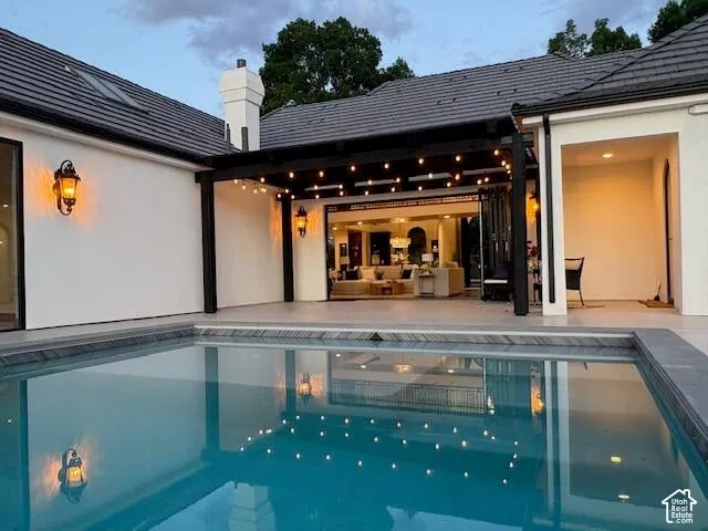 Rear view of property with an outdoor pool, a patio, a chimney, and stucco siding