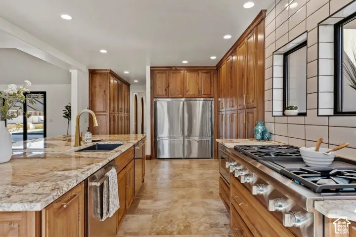 Kitchen featuring wood finish cabinets, stainless steel appliances, recessed lighting, light stone counters, and a center island with sink