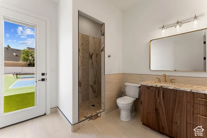 RV Garage Full Bathroom featuring vanity, a marble finish shower, tile walls, and wainscoting