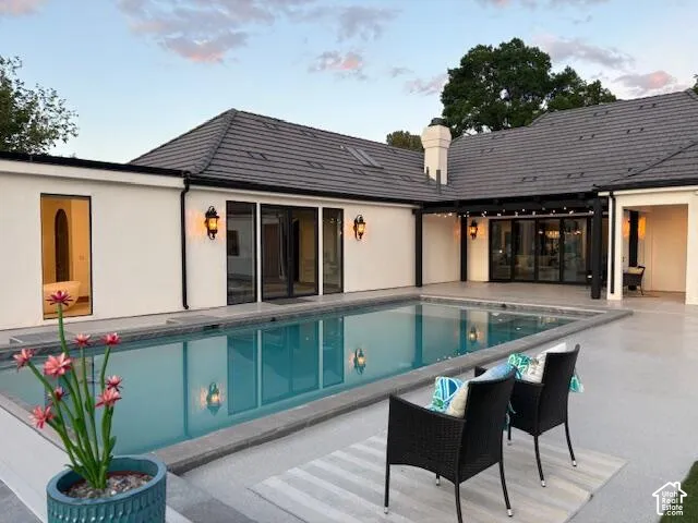 Rear view of property with a patio area, an outdoor pool, a chimney, and stucco siding