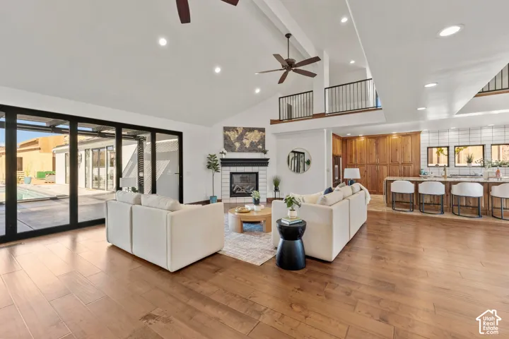 Living room with light wood-style flooring, a glass covered fireplace, recessed lighting, a ceiling fan, and vaulted ceiling