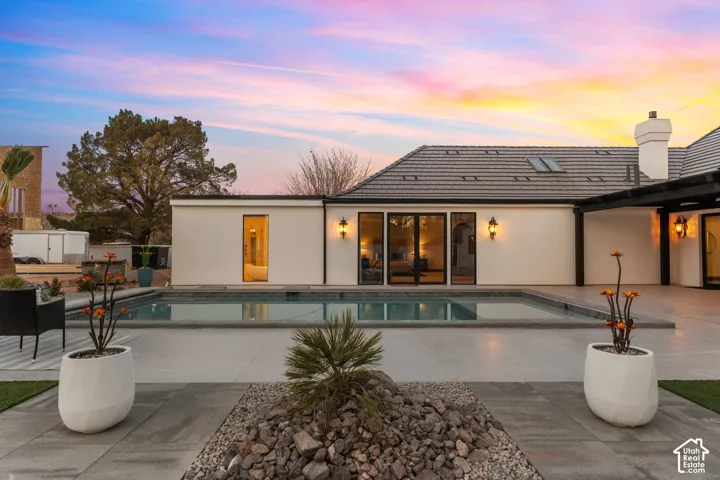 Back of property at dusk featuring a patio, an outdoor pool, a chimney, stucco siding, and a tiled roof