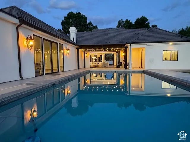 Back of house at dusk featuring a patio area, a chimney, and an outdoor pool