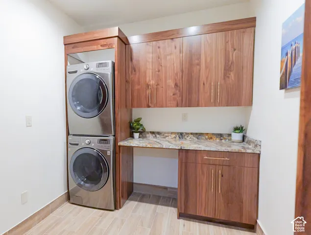 Main Laundry area with stacked washer and dryer, wood finish floors, and cabinet space
