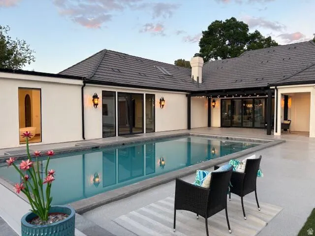 Rear view of property with a patio area, an outdoor pool, a chimney, and stucco siding
