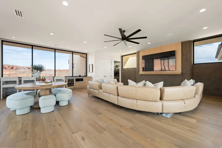 Living area featuring light wood-type flooring, expansive windows, ceiling fan, recessed lighting, and beverage cooler