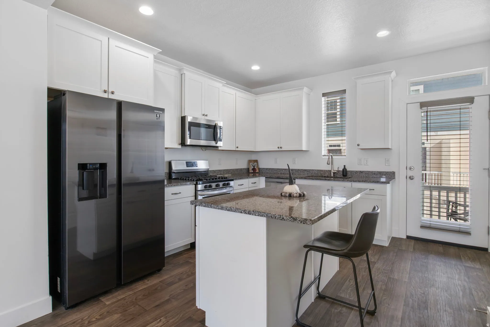 Kitchen with stainless steel appliances, dark stone counters, white cabinetry, a breakfast bar area, and a kitchen island