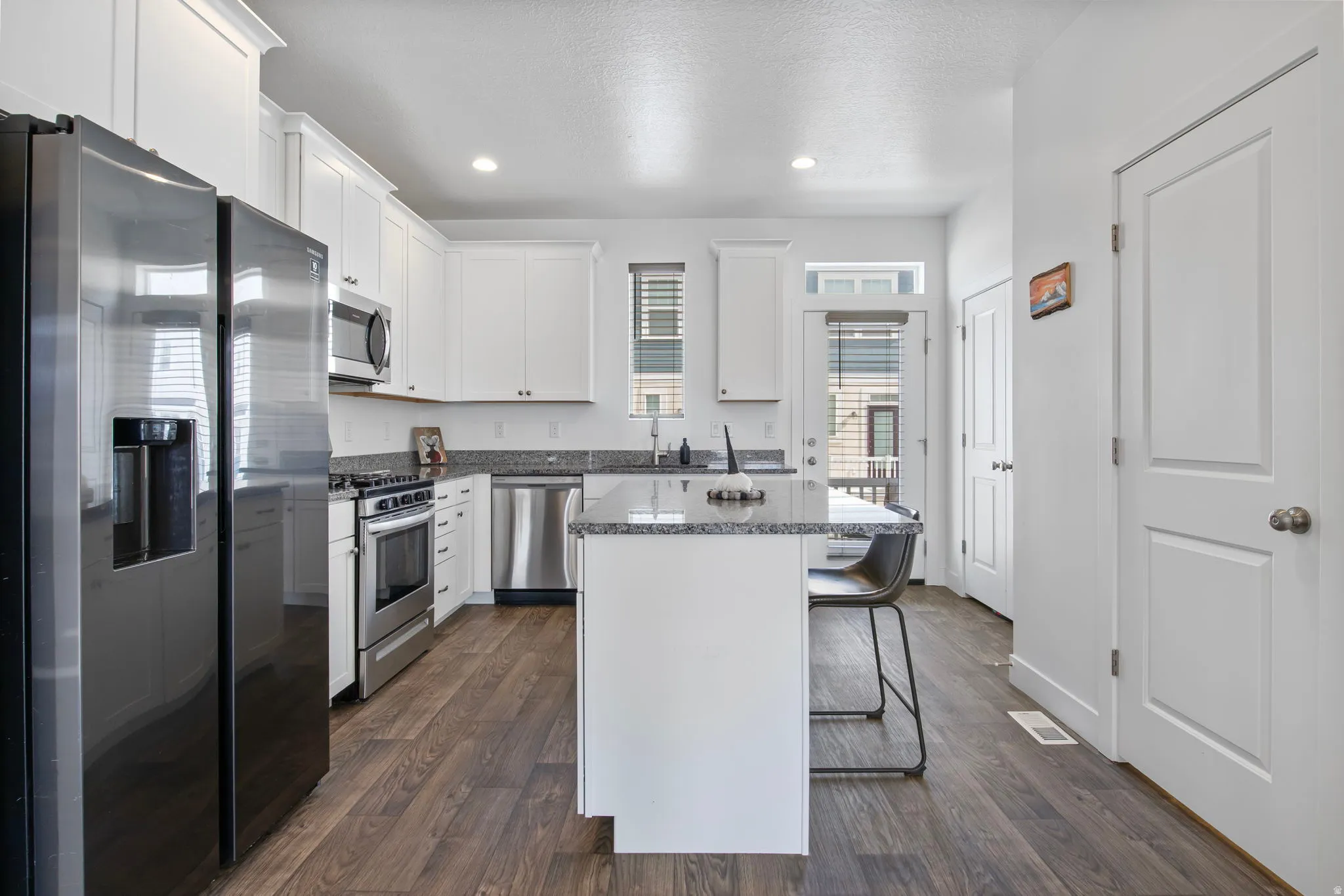 Kitchen with stainless steel appliances, a kitchen bar, a kitchen island, white cabinetry, and dark wood-style floors