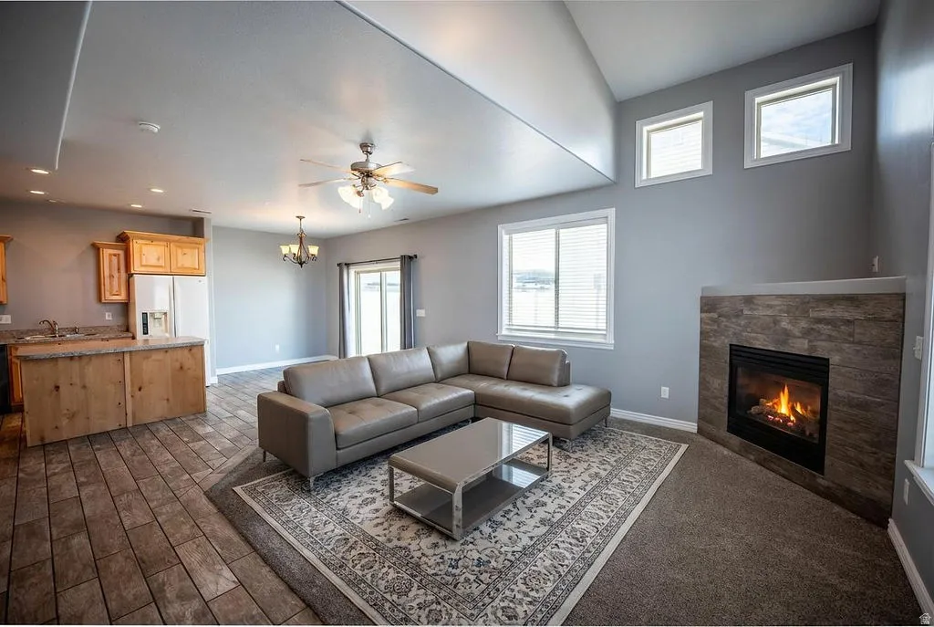 Living room with a tiled fireplace, a ceiling fan, hanging lights, and dark wood-style flooring
