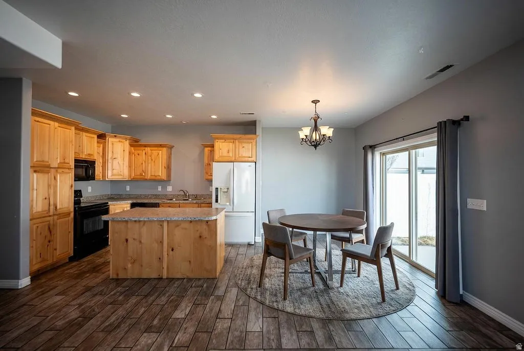 Kitchen featuring black appliances, hanging lights, a kitchen island, dark wood-style floors, and light wood finish cabinets