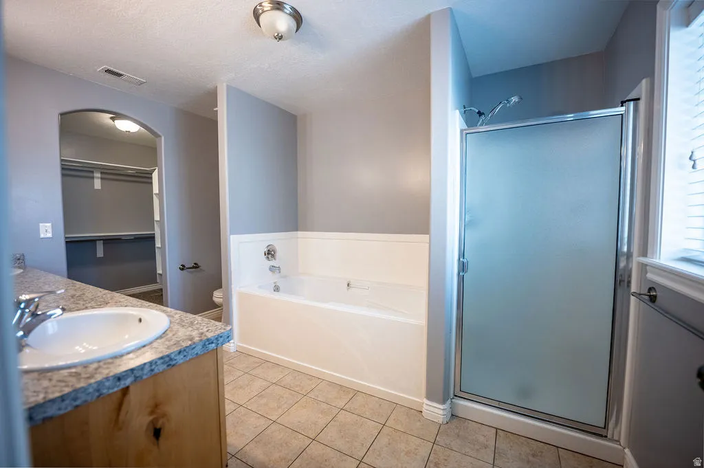 Bathroom featuring a walk in closet, vanity, a garden tub, a stall shower, and a textured ceiling