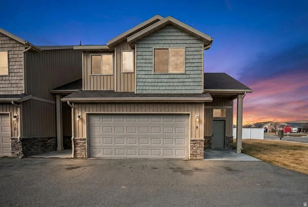 View of front facade with a garage, stone siding, asphalt driveway, and board and batten siding