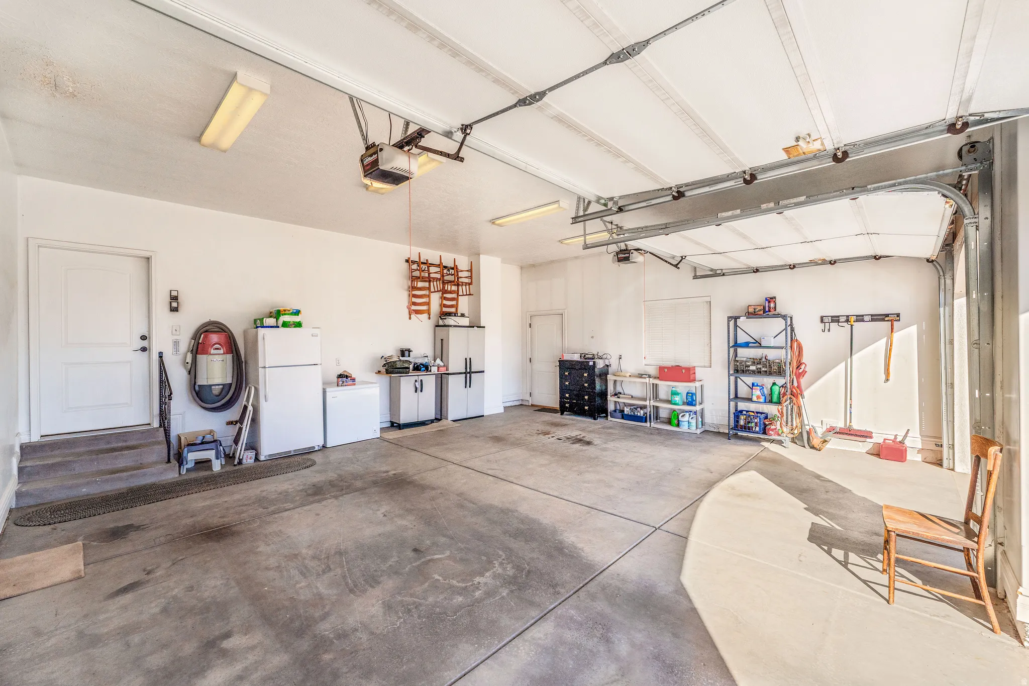 Garage with freestanding refrigerator, white refrigerator, and a garage door opener