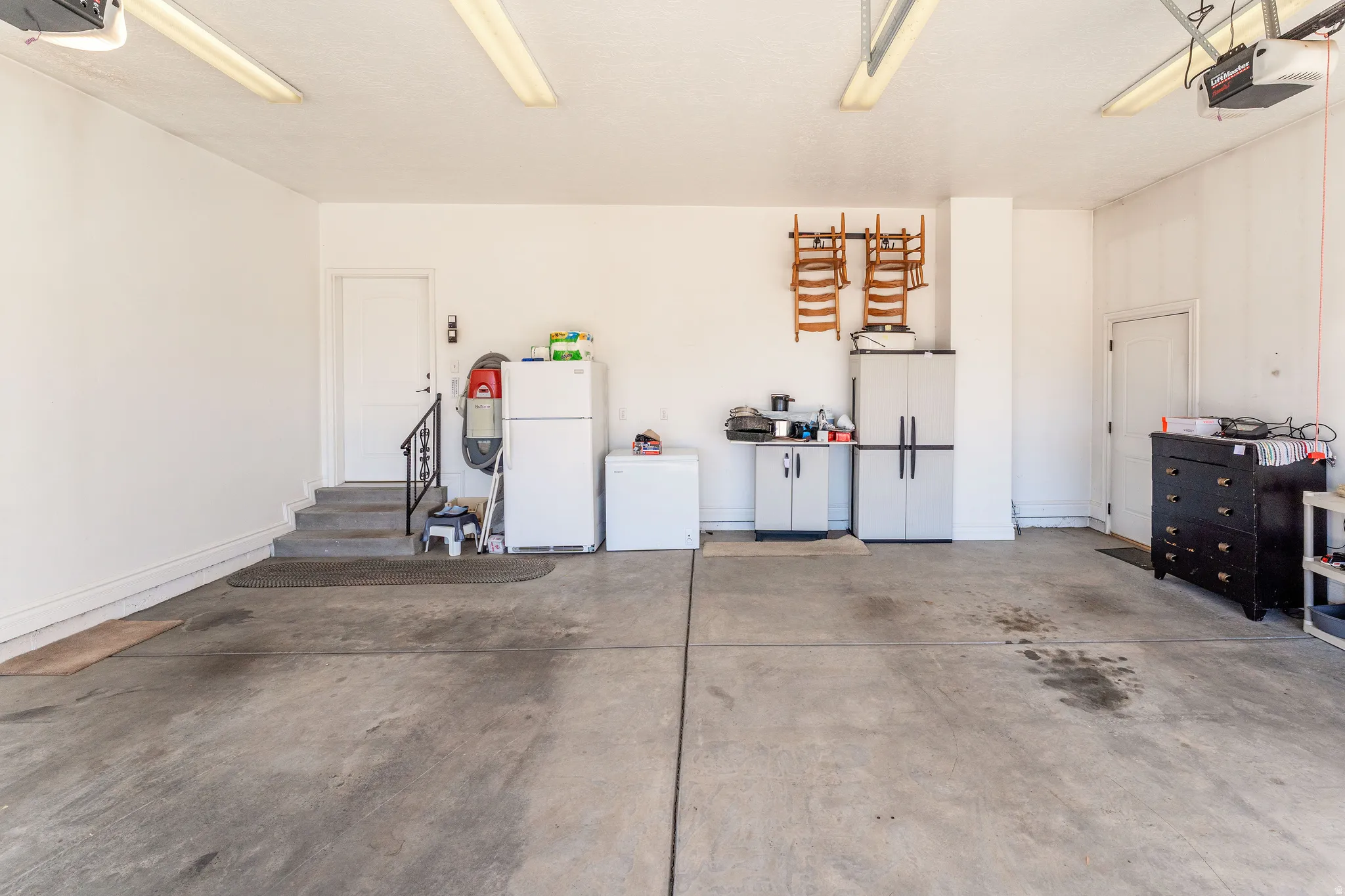 Garage featuring freestanding refrigerator, white refrigerator, and a garage door opener