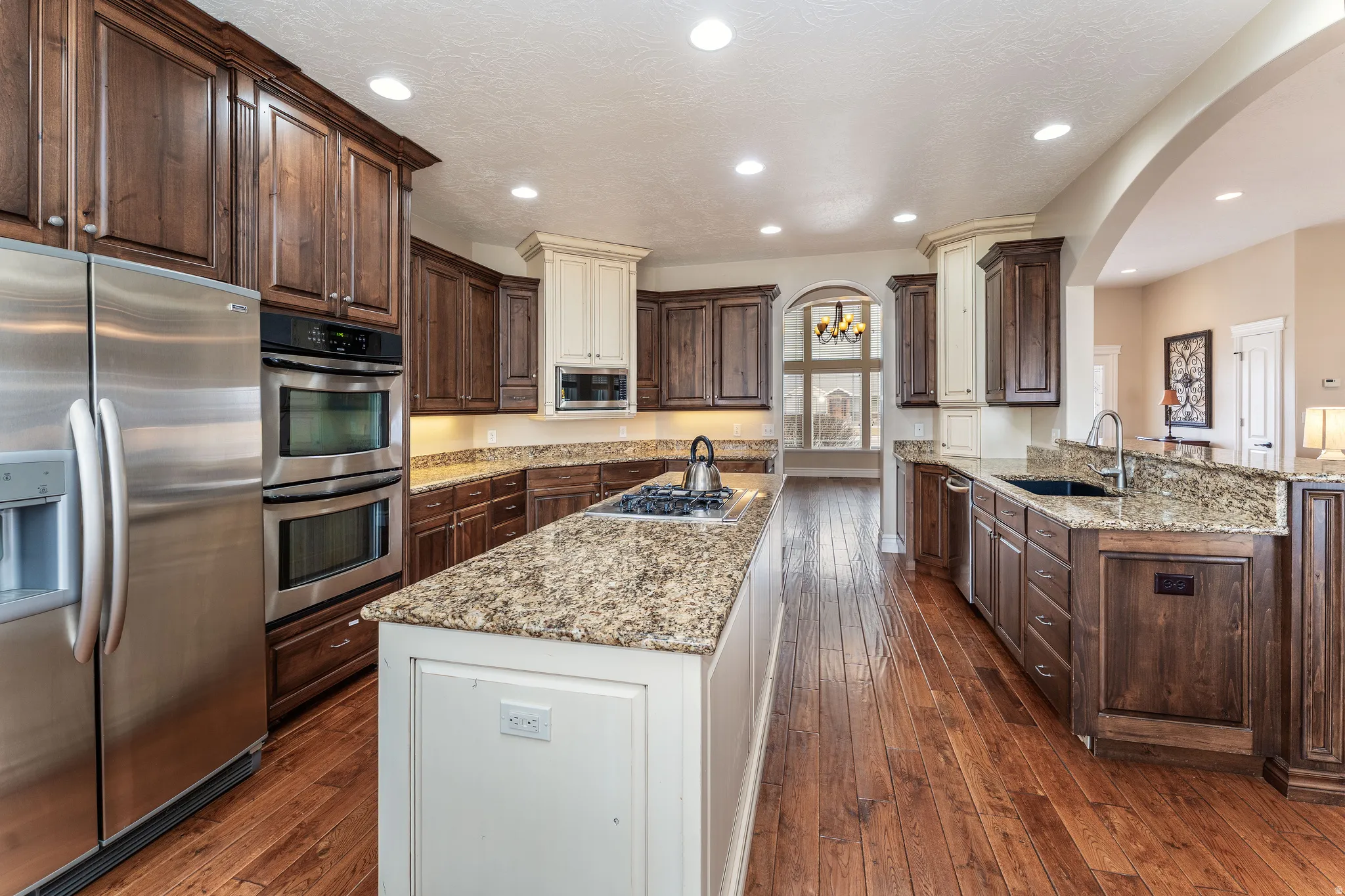 Kitchen with stainless steel appliances, two tone cabinets, light stone countertops, dark wood-type flooring, and hanging lights