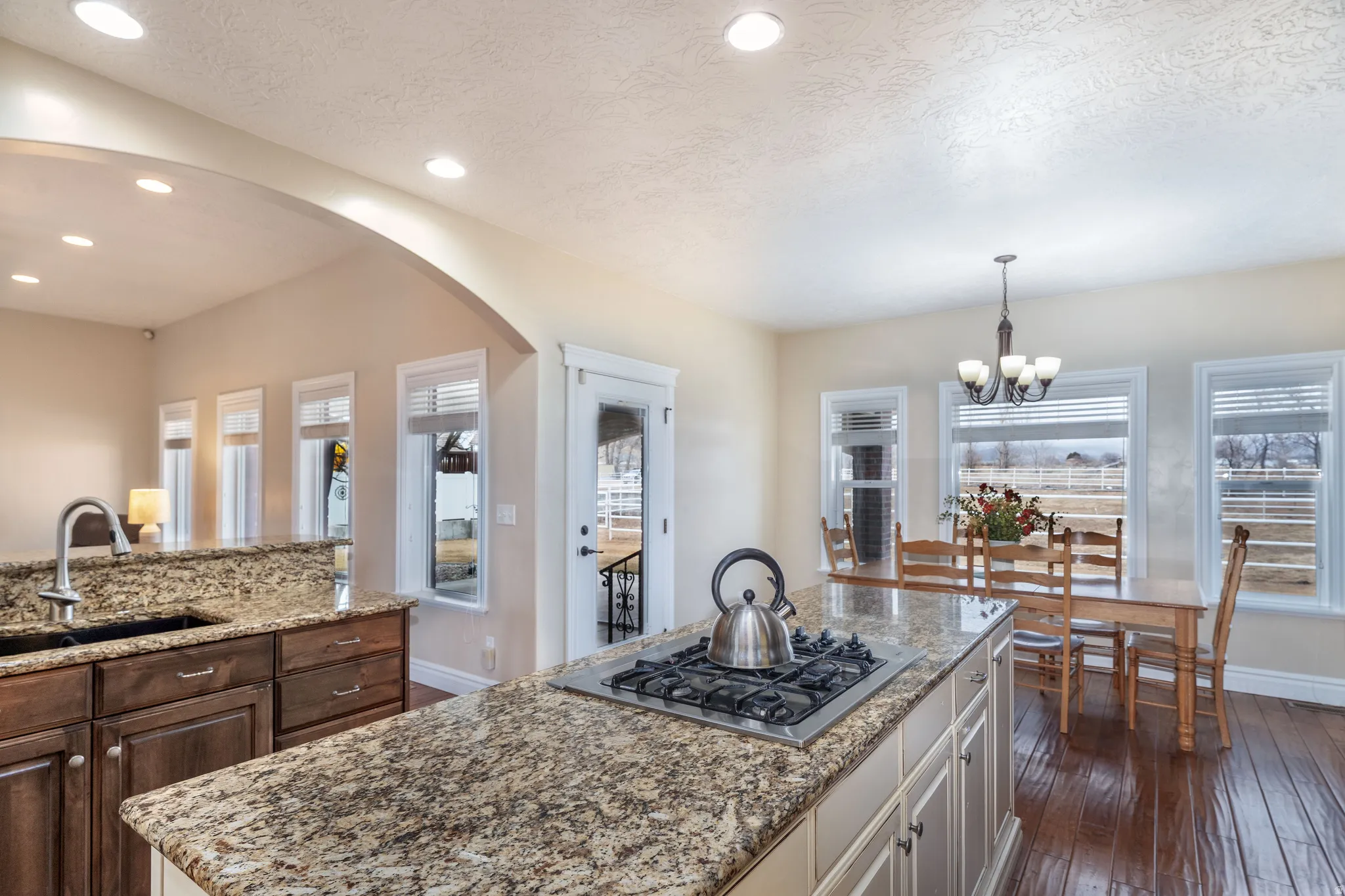 Kitchen featuring a center island, arched walkways, light stone counters, a textured ceiling, and stainless steel gas stovetop