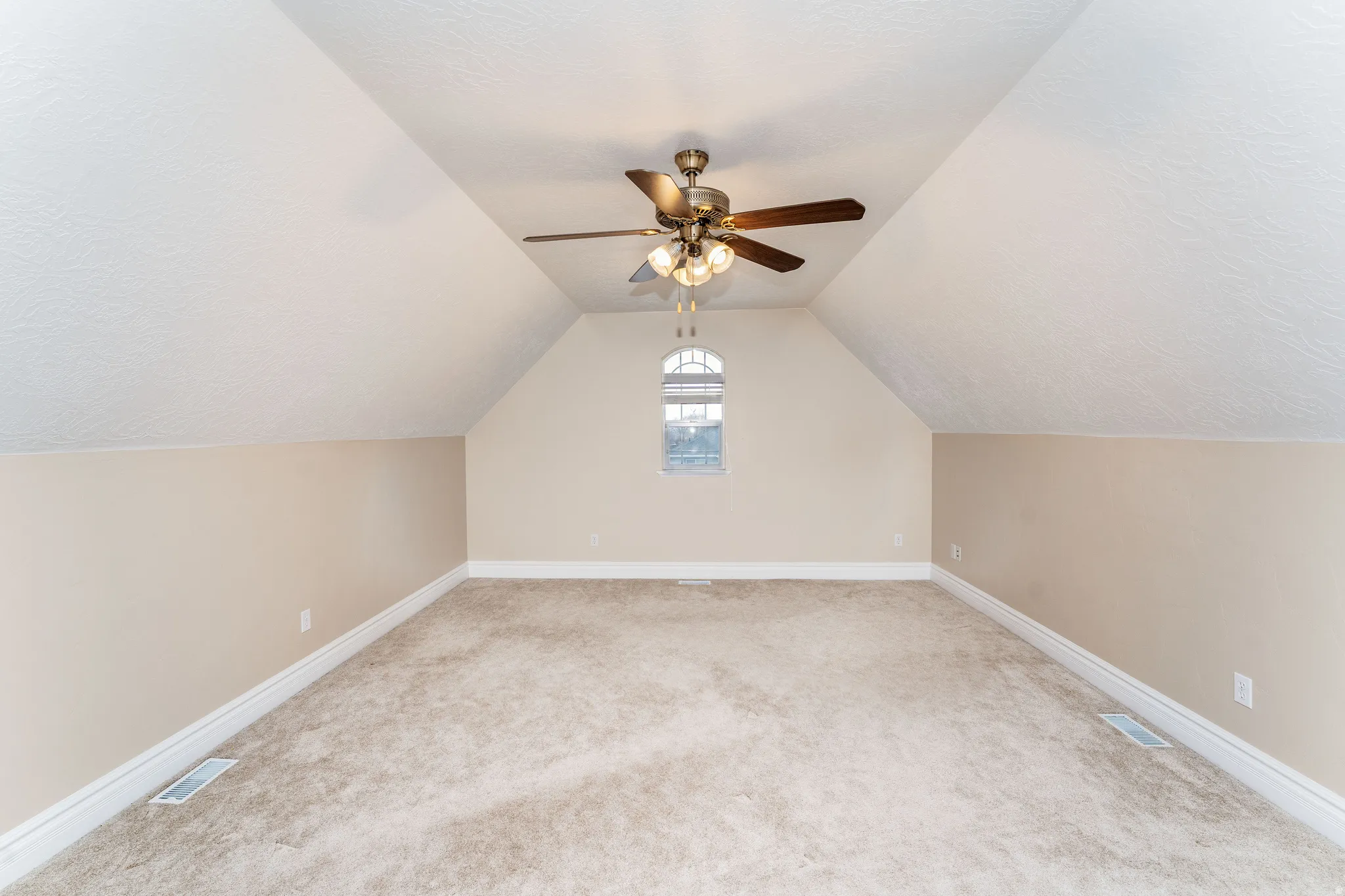 Additional living space with light colored carpet, a ceiling fan, and a textured ceiling