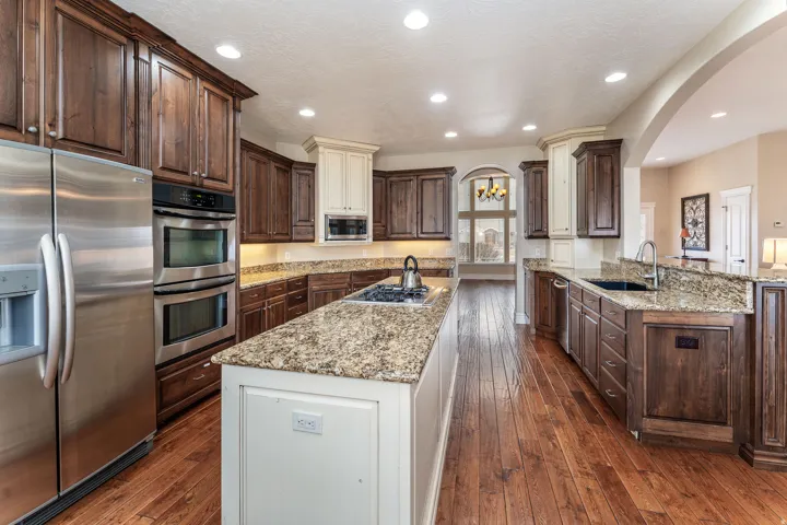 Kitchen with stainless steel appliances, two tone cabinets, light stone countertops, dark wood-type flooring, and hanging lights