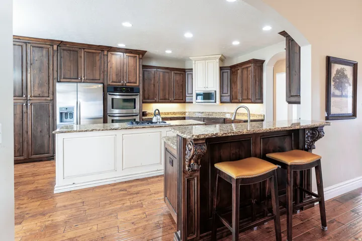 Kitchen featuring two tone cabinetry, light stone countertops, stainless steel appliances, recessed lighting, and light wood-type flooring