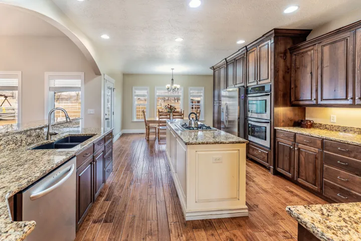 Kitchen with dual tone cabinetry, light stone counters, stainless steel appliances, dark wood-type flooring, and a textured ceiling